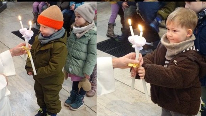 Kinder, die während einer Kirchenzeremonie brennende Kerzen halten, umgeben von aufmerksamen Erwachsenen.