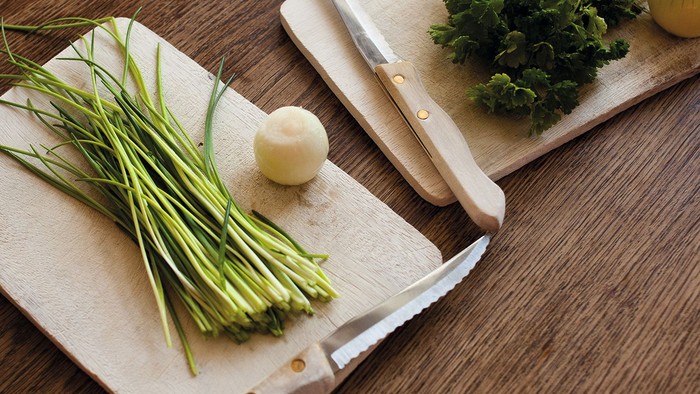 Frische Frühlingszwiebeln, Knoblauchzehen und Petersilie auf Holzschneidebrettern mit einem Messer.