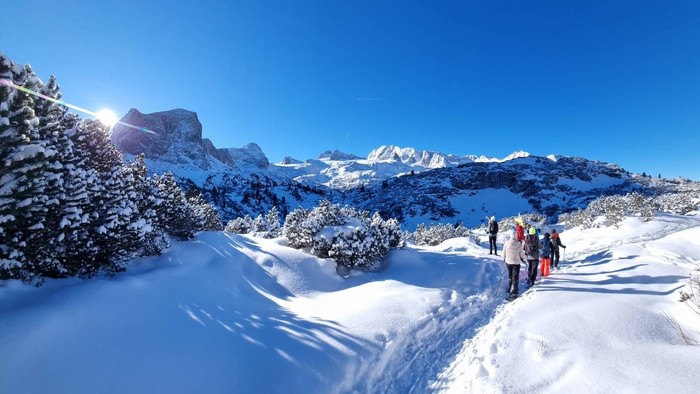 Eine Gruppe wandert auf einem schneebedeckten Bergpfad unter klarem, strahlendem Himmel.