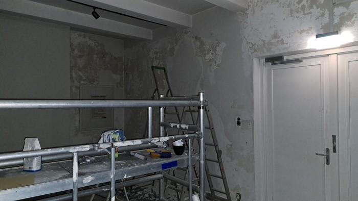 Renovierungsraum mit Gerüst, abblätternder Wandfarbe und verstreuten Baumaterialien.