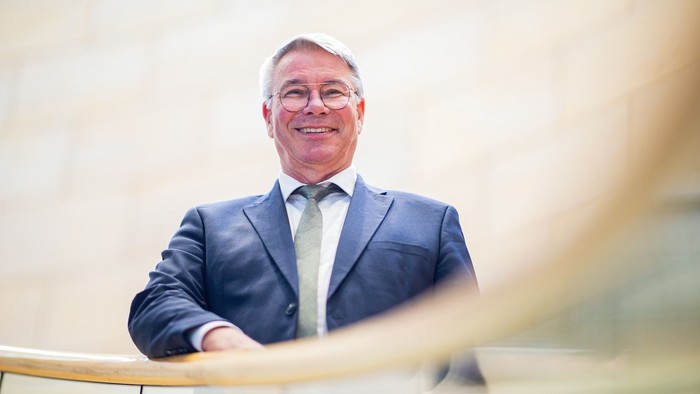 Ein Mann mit Brille und blauem Anzug steht an einem Treppengeländer und lächelt