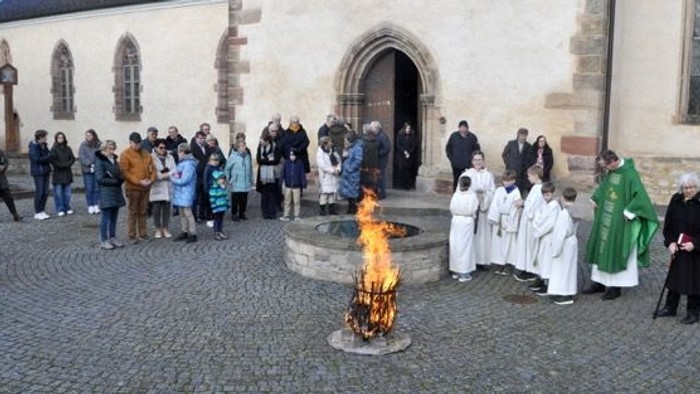 Die Gruppe versammelt sich um ein zeremonielles Feuer, mit Geistlichen in Roben und Teilnehmern in einem Außenhof.