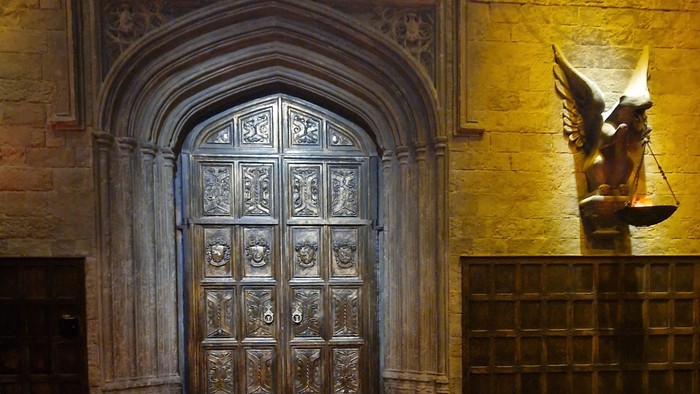 Historische Steinkammer mit verzierter Bogentür und geflügelter Statue an einer Holzpaneel-Wand.