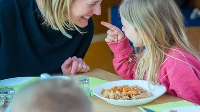 Eine Frau und ein Mädchen sitzen an einem Tisch mit Tellern voller Essen und unterhalten sich.