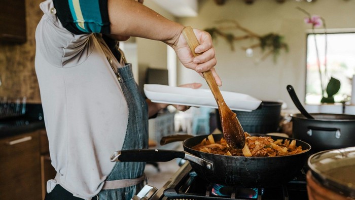 Eine Person rührt in einer Pfanne auf dem Herd und richtet frisch gekochtes Essen an.