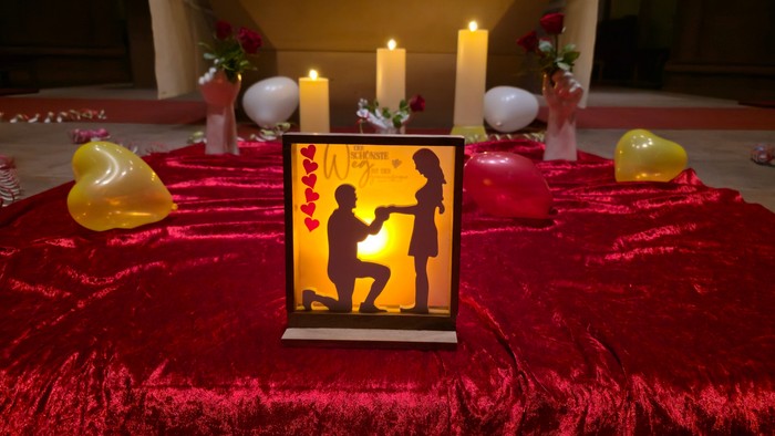 Romantische Tischdekoration mit Silhouettenkerze, herzförmigen Dekorationen und brennenden Kerzen vor einem roten Samt-Hintergrund.