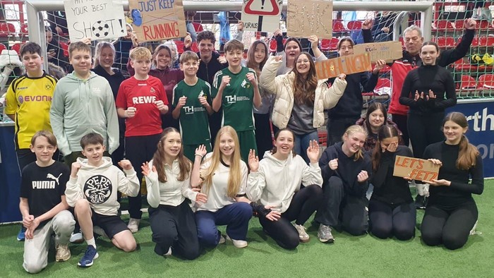 Eine Gruppe von Schüler:innen und Trainer:innen posiert fröhlich gemeinsam bei einer Sportveranstaltung.