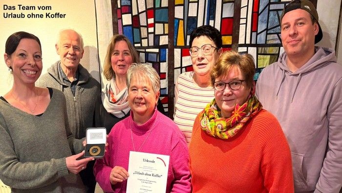 Sieben Personen halten eine Urkunde und einen goldenen Kompass freudig in die Kamera. 