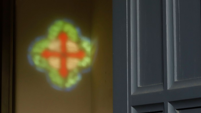 Ein farbiges Kreuz wird auf eine beigefarbene Wand projiziert, neben einer grauen Tür.