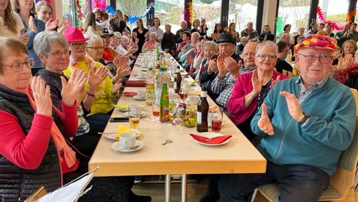 Eine lebhafte Gruppe von Menschen klatscht und feiert an einem festlichen, langen Gemeinschaftstisch.