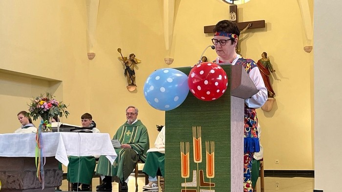 Eine Person in Kostüm hält übergroße Punktballons während eines Gottesdienstes.