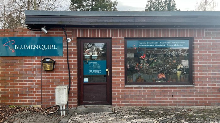 Ein Ziegelsteingebäude-Eingang für Blumenquirl mit Blumenarrangements und Informationsplakaten neben der Tür.