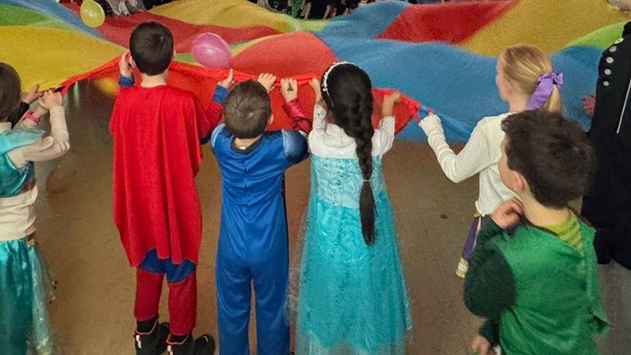 Kinder stehen an einem Fallschirm und flattern mit ihm. Sie sind alle verkleidet