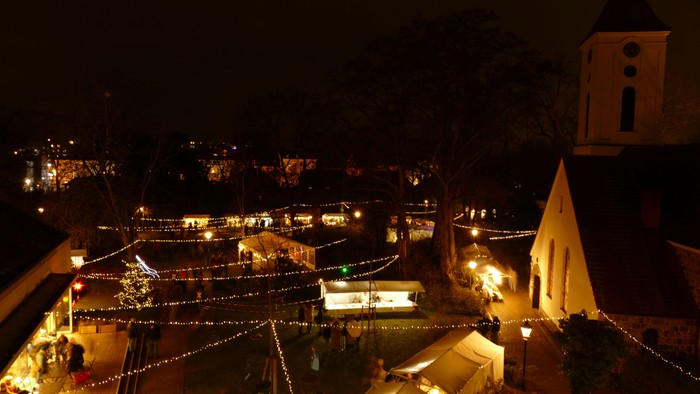 Der Gemeindegarten im Dunklen. Der Turm der Dorfkirche im Hintergrunde und Lichterketten, die die Szene erleuchtet.