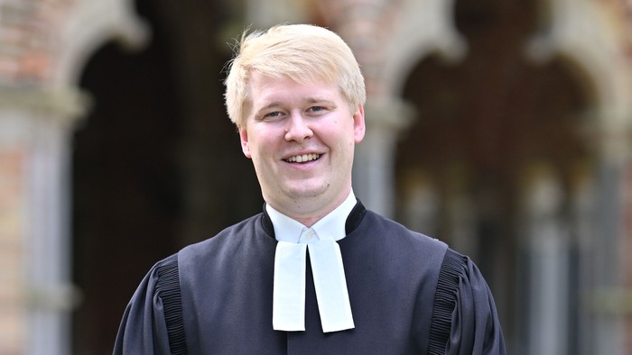 Per Olsen in Robe, draußen vor dem Eingang vom Dom zu Lübeck mit Bogenfenstern lächelnd.