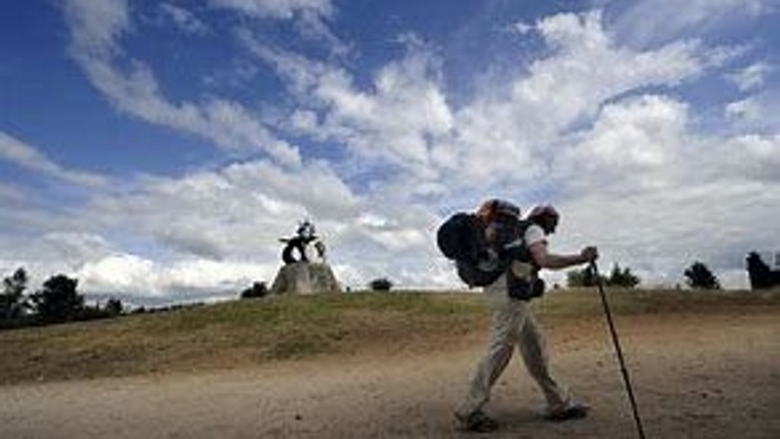 A person hiking with a backpack and walking stick on a dirt path.