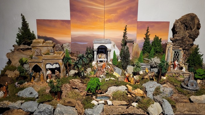 Komplexe Weihnachtskrippe mit detaillierten Figuren, Ruinen und malerischer Sonnenuntergangskulisse.