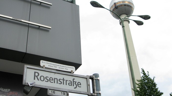 Straßenschild "Rosenstraße" vor modernem Gebäude und hoher Laterne