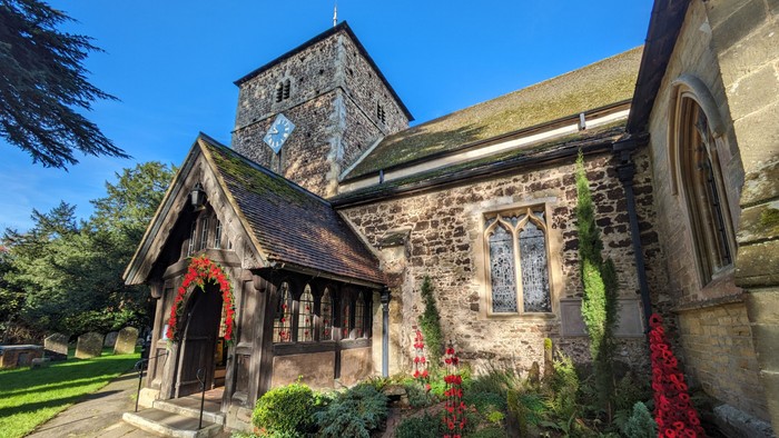 Historic stone church adorned with festive greenery and red flowers, featuring a quaint porch entrance.