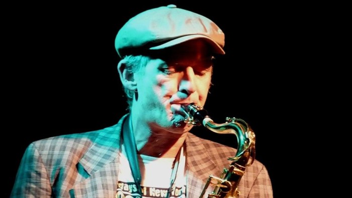 Ein Mann mit Mütze spielt mit konzentrierter Intensität Saxophon auf der Bühne.