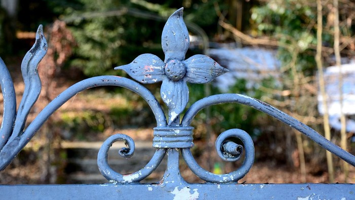 Eisiger Zaun mit filigranem Blumenmuster im Vordergrund, unscharfer Garten im Hintergrund