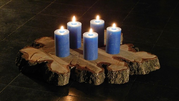 Vier blaue Kerzen brennen auf einer geschnitzten hölzernen kreuzförmigen Platte.