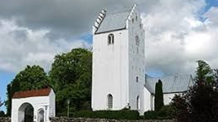 Et hvidt tårn med spids tak og en mur omgivet af træer og en vej.