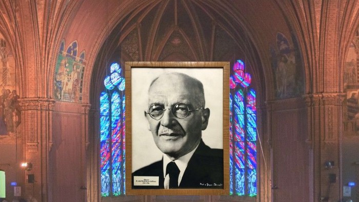 Ein gerahmtes Porträt hängt in einer prächtigen Halle mit Buntglasfenstern und verzierten Dekorationen.