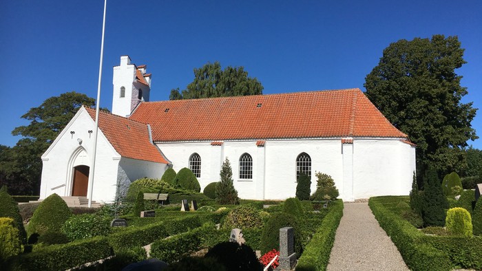 En smuk hvid kirke med rødt tag og en lang gravelæssede adgangsvej