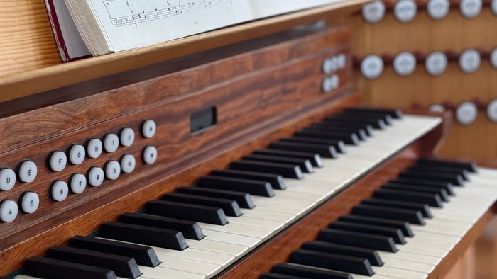 Et nærbillede af et orgelmanual med noder og betjeningsknapper i baggrunden.