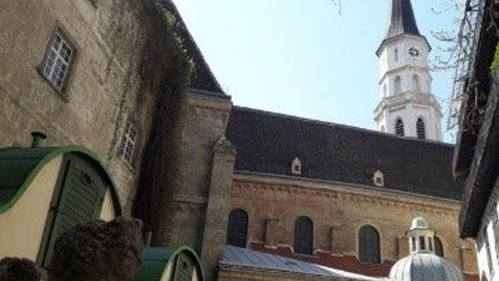 Historisches Gebäude mit hohem Uhrturm und einem grünen Bogentor in einem Innenhof.