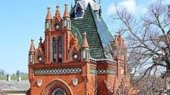 Verzierte Backsteinkirche mit aufwendiger gotischer Architektur und grünen Türmen unter klarem Himmel.