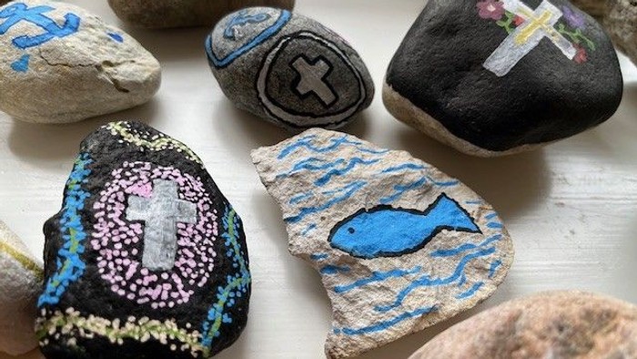 Malerede sten med kors, fisk og blomstermotiver arrangeret på en overflade.