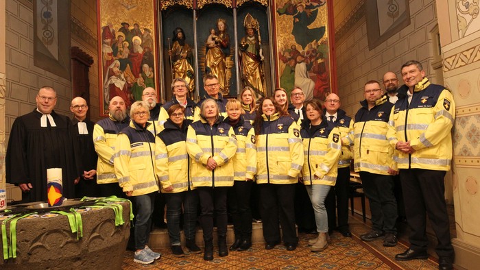 Gruppe von Einsatzkräften in gelben Uniformen, die sich mit Geistlichen in einem geschmückten Kircheninneren fotografieren lassen.