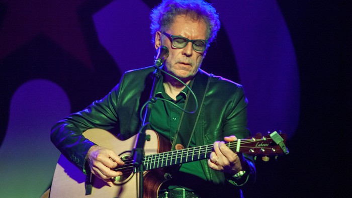Ein Mann mit Brille spielt auf der Bühne eine akustische Gitarre unter blauem Licht.