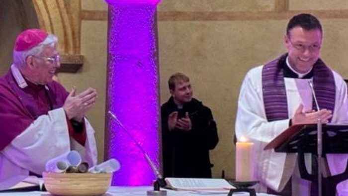 Religiöse Zeremonie in einer Kirche mit Geistlichen, die ein Ritual nahe beleuchteten Altarsäulen durchführen.