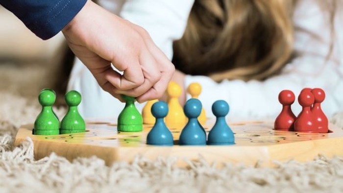 Ein Kind spielt mit bunten Holzsteckfiguren auf einem Spielbrett.