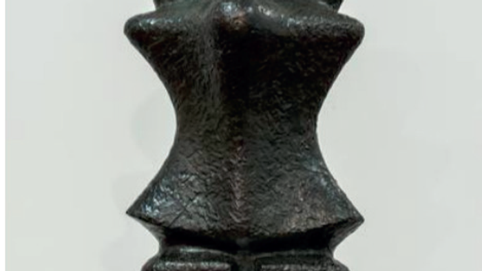 Abstrakt sort skulptur med en stiliseret, tekstureret menneskelignende figur med brede skuldre og en minimalistisk holdning.