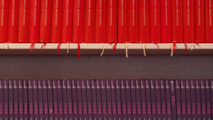 Gestapelte rote und violette gebundene Bücher, mit Schnur zusammengebunden, in geordneten Reihen angeordnet.