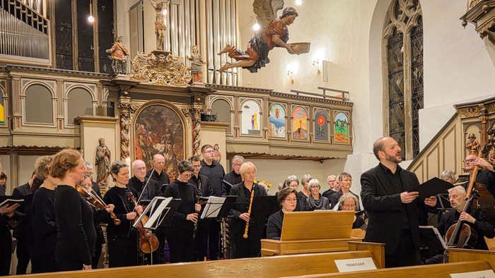 Ein Solist singt in einer Kirche, vor einem Chor und Orchester stehend