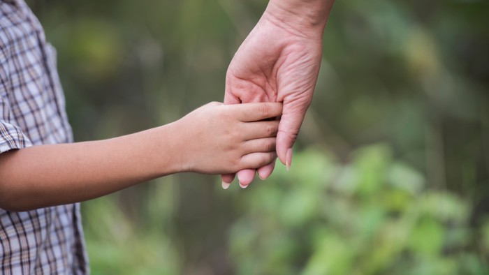 Kind wird von einer Frau an die Hand genommen
