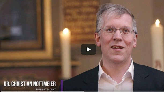 Ein Mann in Anzug und Krawatte spricht vor einem Altar mit Kerzen.