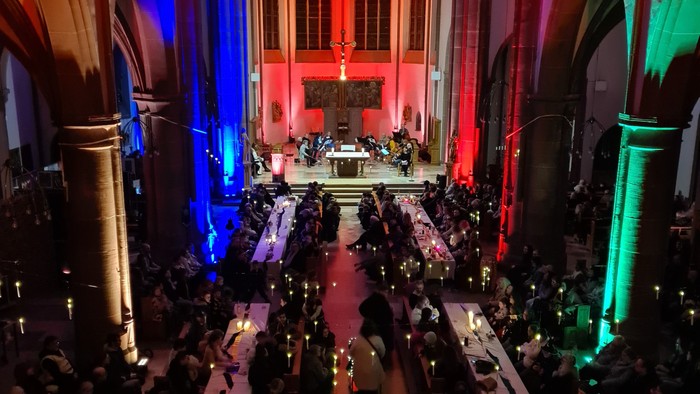 Bunt beleuchtete Kathedrale beherbergt eine große Versammlung mit einer feierlichen Zeremonie und sitzenden Teilnehmern.