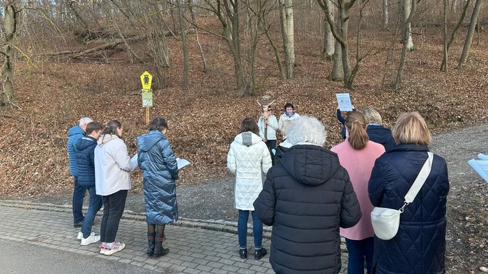 Eine Gruppe von Menschen versammelte sich im Freien in einem bewaldeten Gebiet und hörte einem Guide zu, während in der Nähe informative Schilder aufgestellt waren.