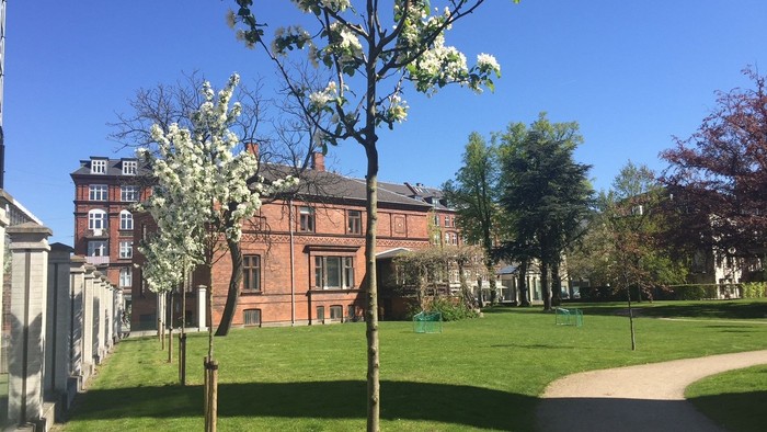 En smuk park med blomstrende træer og et stort rødt hus i baggrunden