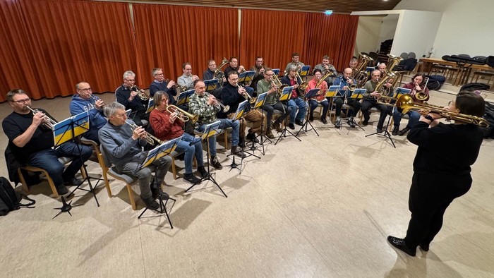 Ein großer Posaunenchor sitzt und spielt in einem Saal