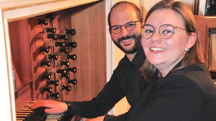 Ein Mann und eine Frau spielen gemeinsam an einer Orgel und lächeln in die Kamera