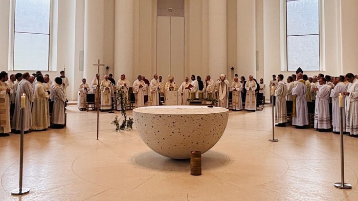 Großer Raum mit vielen Menschen in weißen Roben, Säulen und einem großen Objekt in der Mitte