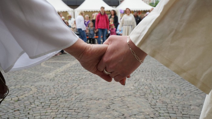 Paar, das sich bei einer Outdoor-Hochzeitszeremonie an den Händen hält, umgeben von Gästen.