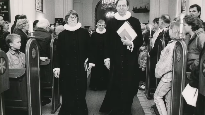 Sort-hvid kirkeoptagelse med gejstlige og menighed, der forlader kirken gennem midtergangen.